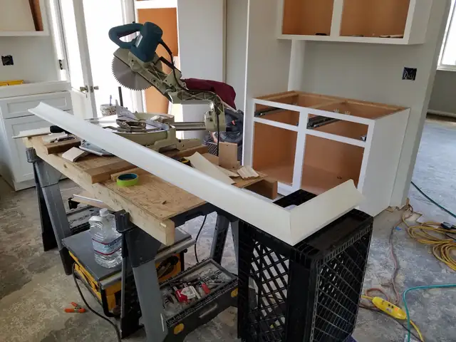 White cabinets and trim being built on site with a miter saw on a work table
